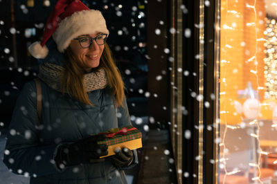 Smiling woman holding christmas gift while standing outdoors