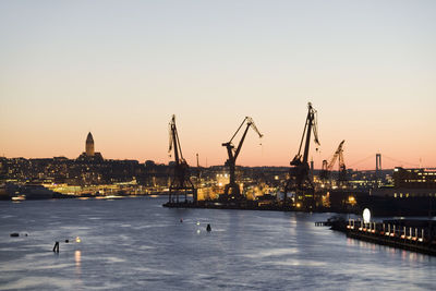 Silhouette cranes at commercial dock by gota canal against clear sky during sunset