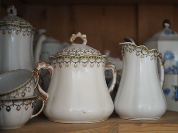 Close-up of antique tea pot and tea cups in wooden cabinet