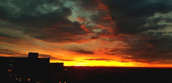 Silhouette buildings against dramatic sky during sunset