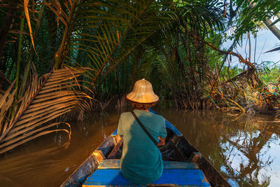 Rear view of man sitting by plants against trees