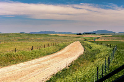 Dirt road amidst field against sky