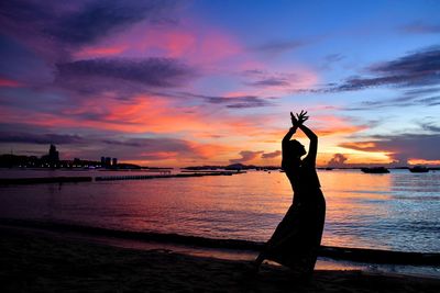 Silhouette woman standing at beach against sky during sunset