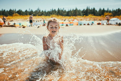 Little girl splashed by sea wave while sitting and playing on a beach. child enjoying the sea