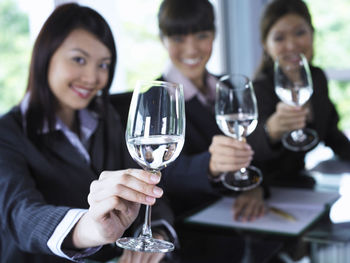 Portrait of businesswomen showing wineglasses at desk