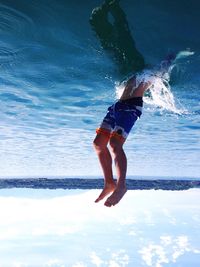 Upside down image of man diving into lake against sky