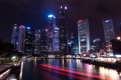 Illuminated buildings by river against sky in city at night