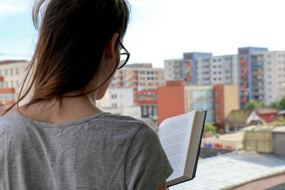 Rear view of woman reading book against buildings