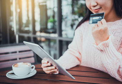 Midsection of woman holding smart phone at cafe