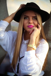 Portrait of young woman wearing hat sitting by tree trunk