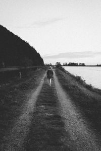 Rear view of people walking on shore by sea against sky