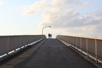 Rear view of friends walking on footbridge against sky