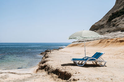 Deck chairs under parasol at beach against clear sky