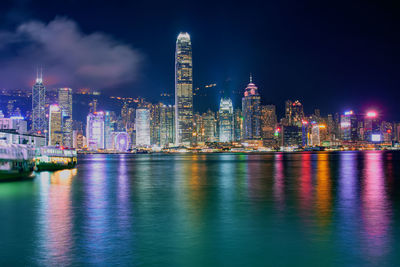 Illuminated buildings by river against sky at night