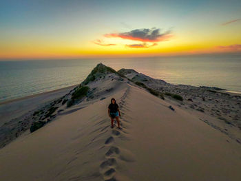 Rear view of people on beach against sky during sunset