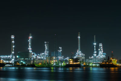 Illuminated factory by river against sky at night