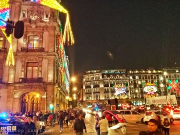 People on illuminated street amidst buildings in city at night