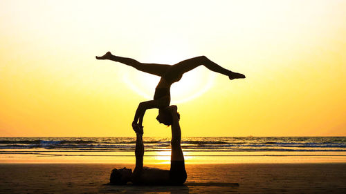 Silhouette man carrying woman while lying on beach against sky during sunset