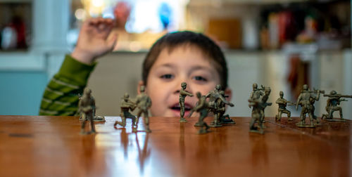 Little boy cheers on toy soldiers as he plays with a pretend battle