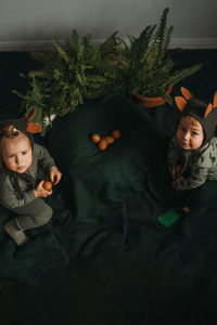 Toddler twins in funny dino costumes sitting with eggs in hands