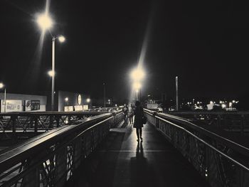 Rear view of woman walking on illuminated street at night