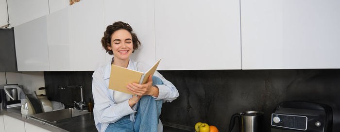 Portrait of smiling young woman standing against wall