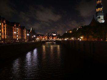 Illuminated buildings by river against sky at night