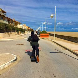 Rear view of man skateboarding on street against sky