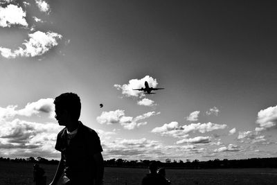 Playful boy on field against airplane flying in sky