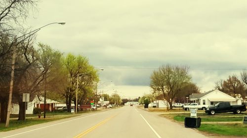 Road amidst trees against cloudy sky