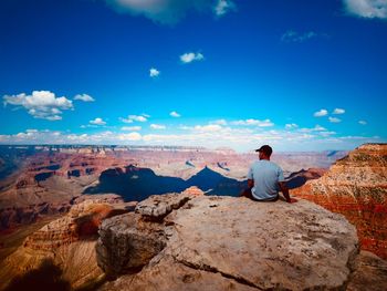 Rear view of woman sitting on rock against blue sky