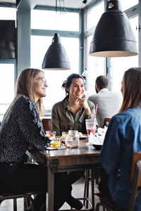 Smiling young female friends sitting at dining table in restaurant