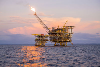 Offshore platform in sea against sky during sunset