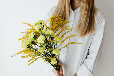 Midsection of woman holding flowers against white background