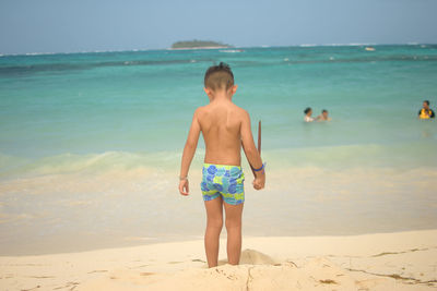 Full length of shirtless boy on beach against sky