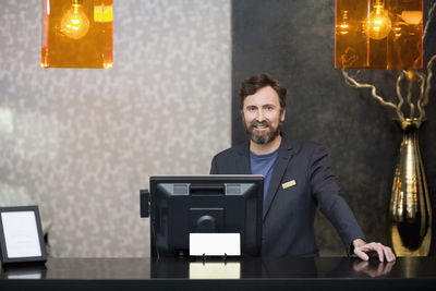 Portrait of confident male receptionist standing at counter in hotel