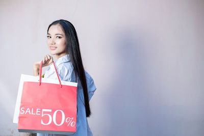 Portrait of a smiling young woman standing against wall