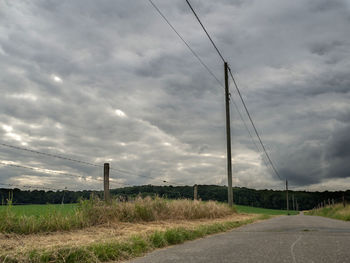 Road passing through field against cloudy sky
