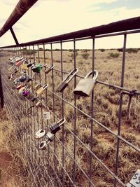 Padlocks hanging on railing by bridge against sky