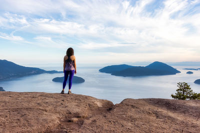 Rear view of woman standing on shore against sky