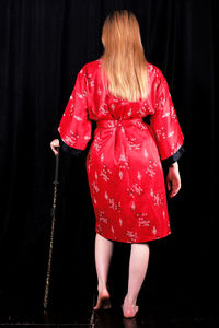 Rear view of woman wearing kimono and holding swords against black background