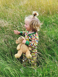 Cute toddler playing in long grass with his teddy