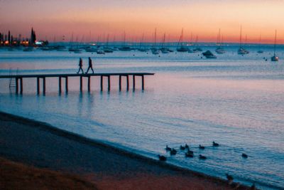 Silhouette people on pier by sea against sky at sunset