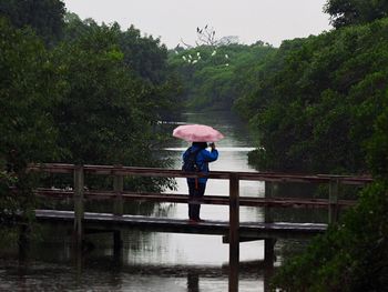 Woman standing on footbridge over river in forest