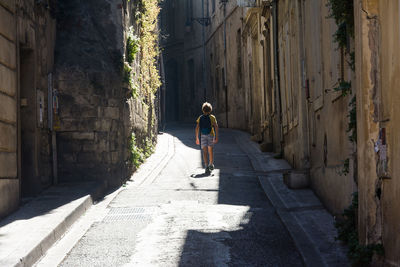 Rear view of man walking on alley amidst buildings in city