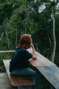 Woman using mobile phone while sitting on tree