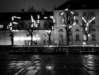 Illuminated street amidst buildings against sky at night