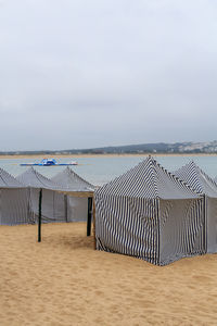 Hooded chairs on beach against sky