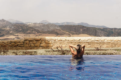 Shirtless woman swimming in pool against landscape