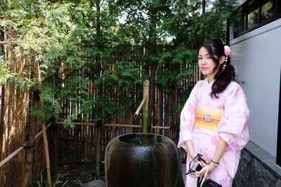 Young woman sitting on seat against trees